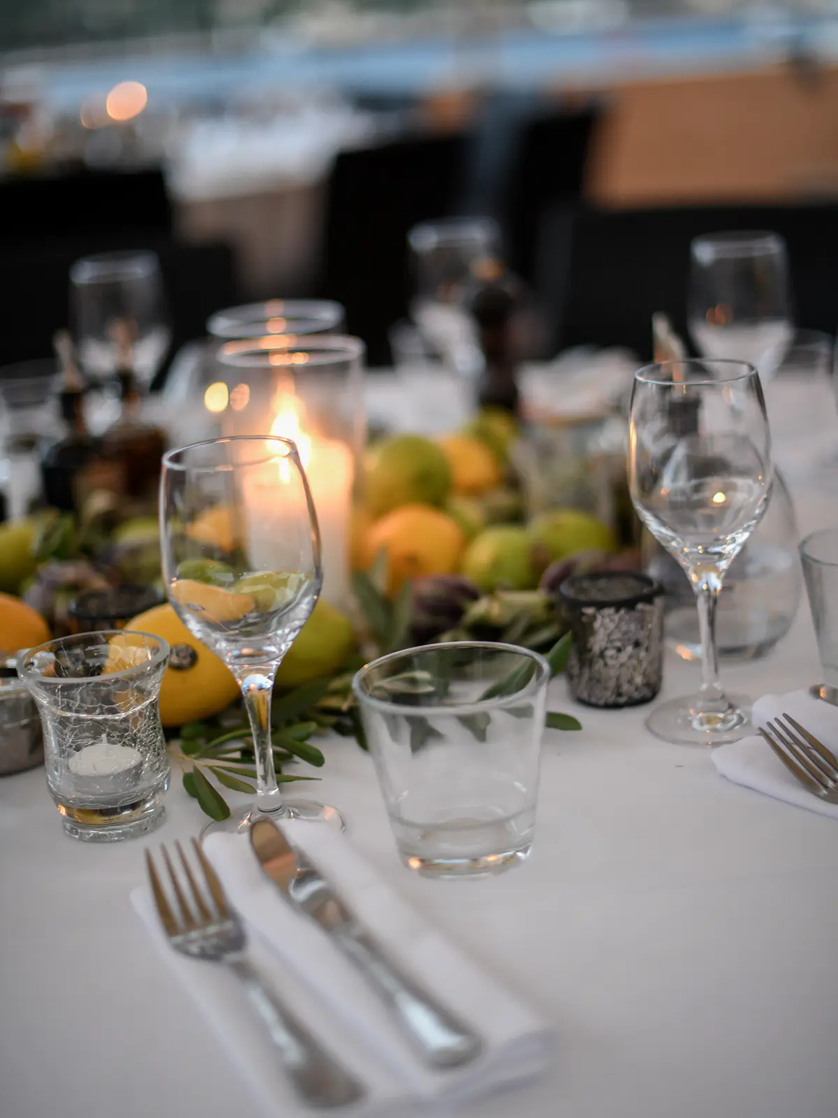 Elegant table setting with wine glasses, silverware, lemons, limes, and candles, creating a warm, inviting atmosphere for an outdoor gathering.